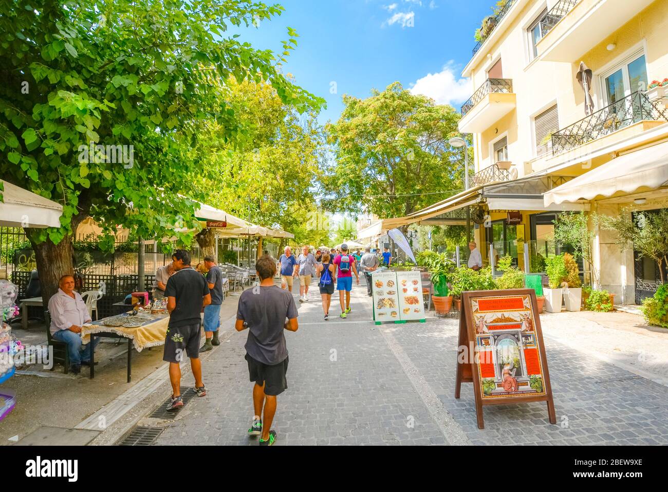 Tourists walk the crowded path past cafes, street vendors and souvenir shops in the Plaka district of Athens, Greece on a summer day Stock Photo