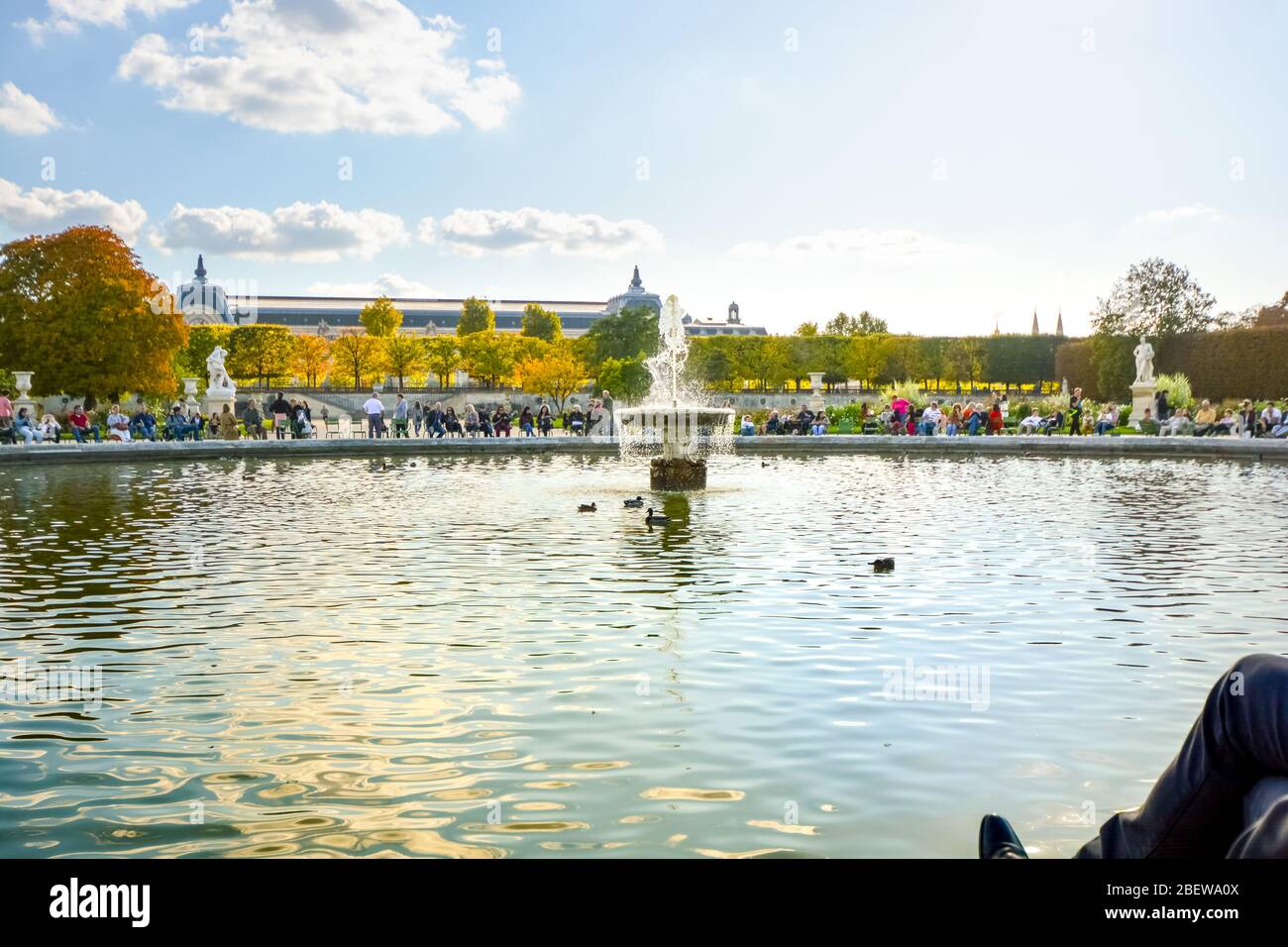 Parisians and tourists enjoy an afternoon at the grand bassin rond, the large water fountain pond at the Tuileries Garden in Paris France Stock Photo