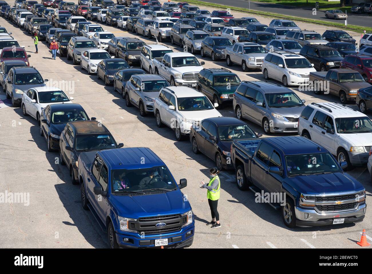 Drivers in hundreds of vehicles wait for Central Texas Food Bank volunteers to deliver 28-pound boxes of staples during a food giveaway in Austin, Texas. Almost 1,500 families picked up boxes in response to extensive coronavirus pandemic job losses and general Texas economic fallout. Stock Photo