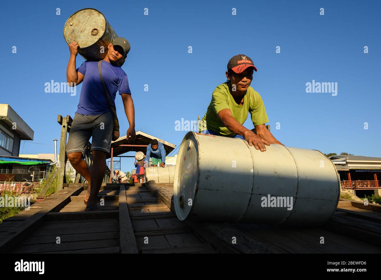 Men carrying and rolling drums to a boat, Pathein, Myanmar Stock Photo