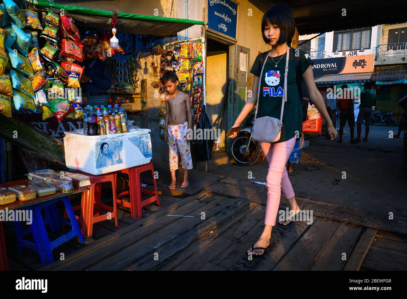 Young woman walking by a shop in the late afternoon, Pathein, Myanmar Stock Photo