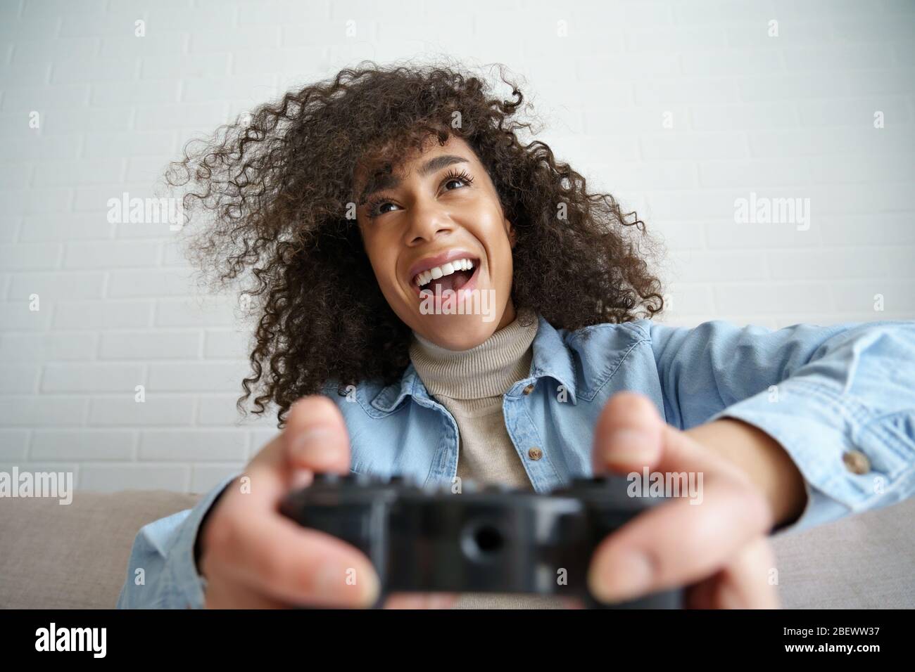 Excited african girl gamer holding joystick controller playing video game. Stock Photo