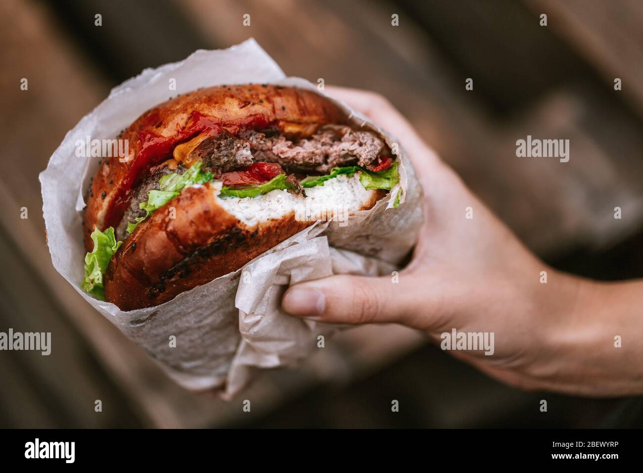 Hand holding a juicy burger. Hamburger in hand. Shallow depth of field Stock Photo