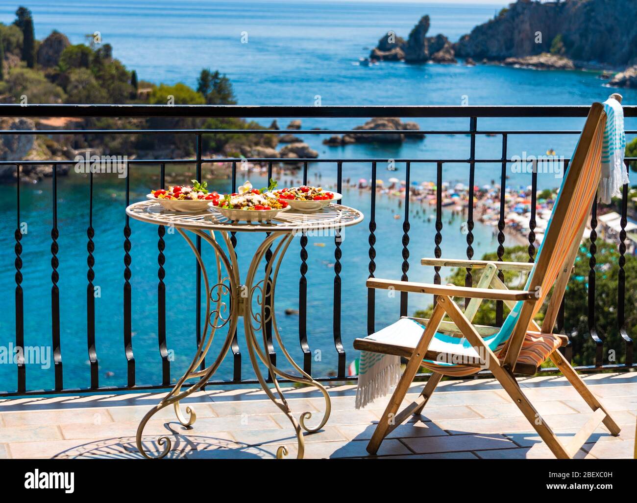 Tasty Italian lunch on a sunny terrace with Incredible sea view of the crowded beach at Isola Bella Nature Reserve, Taormina, Sicily Stock Photo