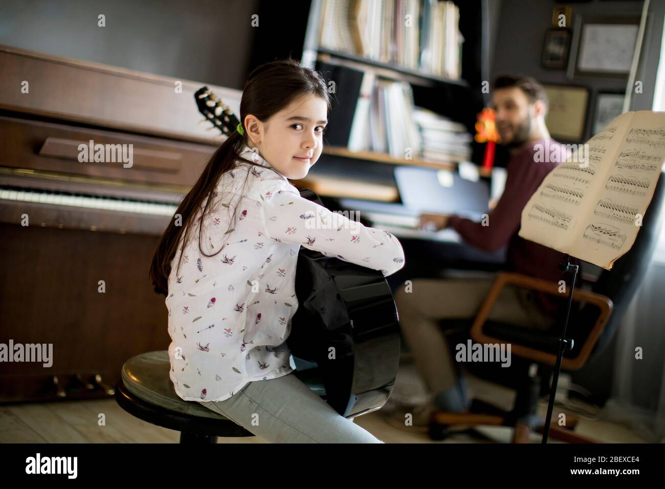 Cute little girl playing guitar with her music teacher in the rustic