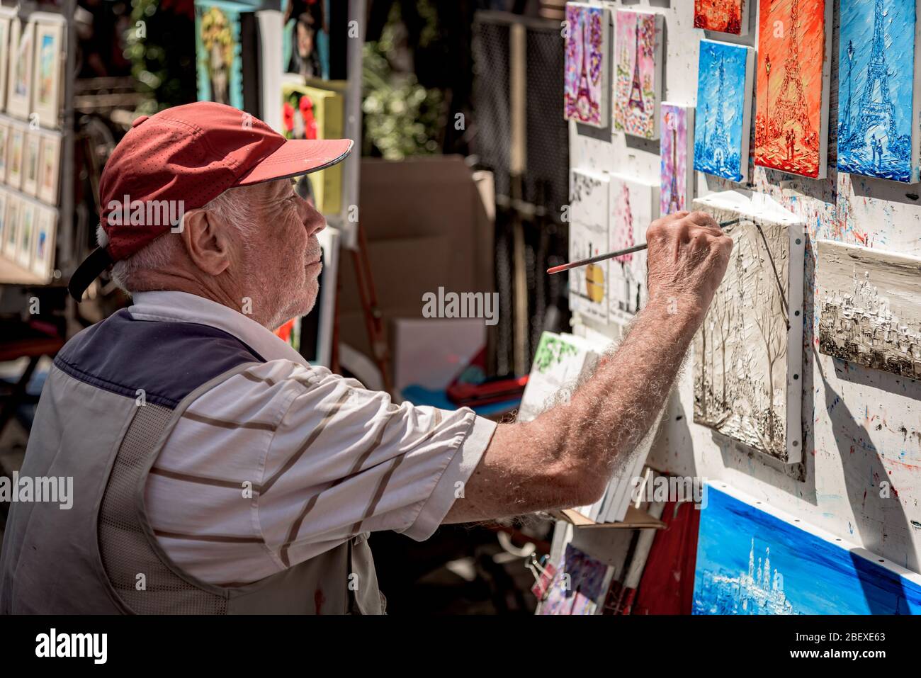 An old man painter works in the open air artist market in Tertre Square (Place du Tertre), Montmartre district near the Basilica of the Sacre Coeur. Stock Photo