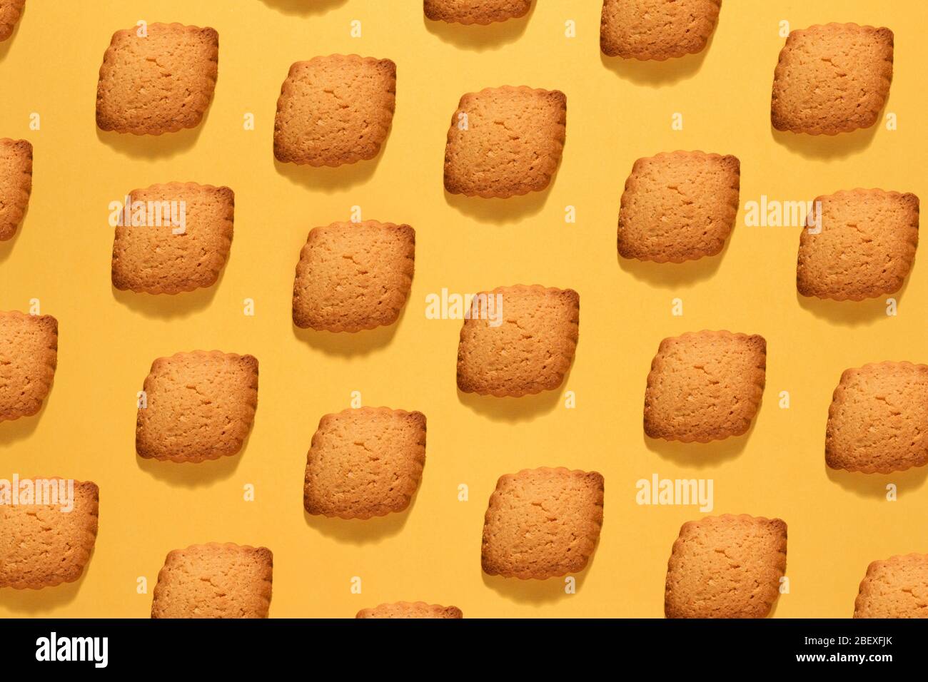 Baking or food still life background of neatly arranged crunchy cookies in diagonal lines on yellow in a full frame view Stock Photo