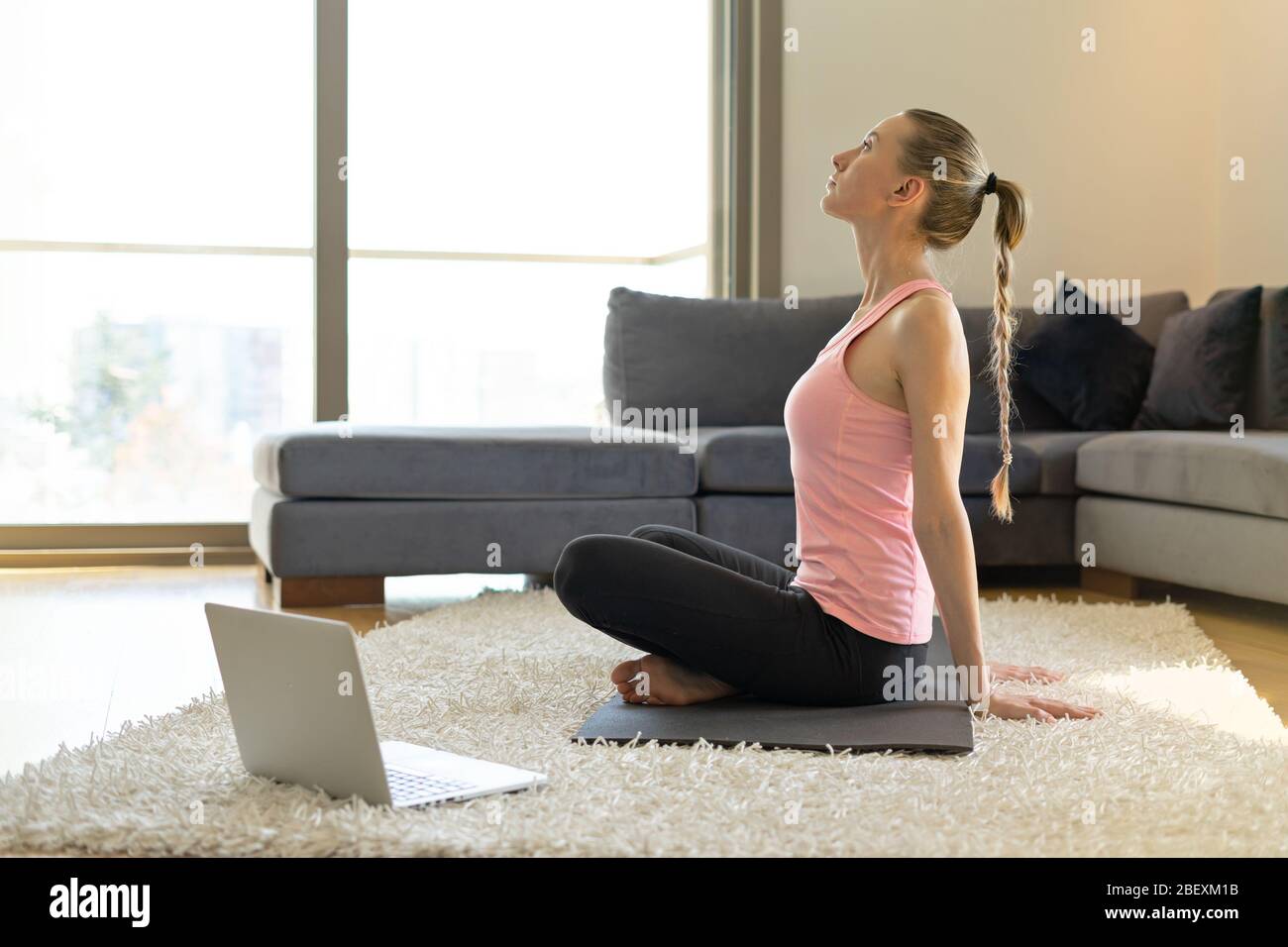 Online sport fitness yoga training. young woman and doing exercises on yoga mat opposite laptop with online master class. training at home Stock Photo