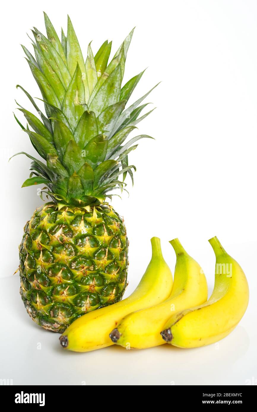 A whole pineapple and three bananas against a plain white background Stock Photo