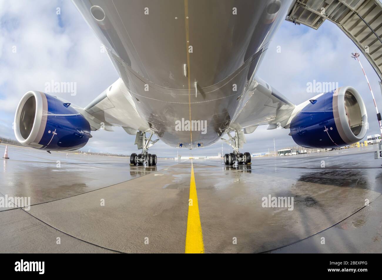 Passenger wide-body plane is parked on the airport apron. Aircraft fuselage, engine and main landing gear Stock Photo