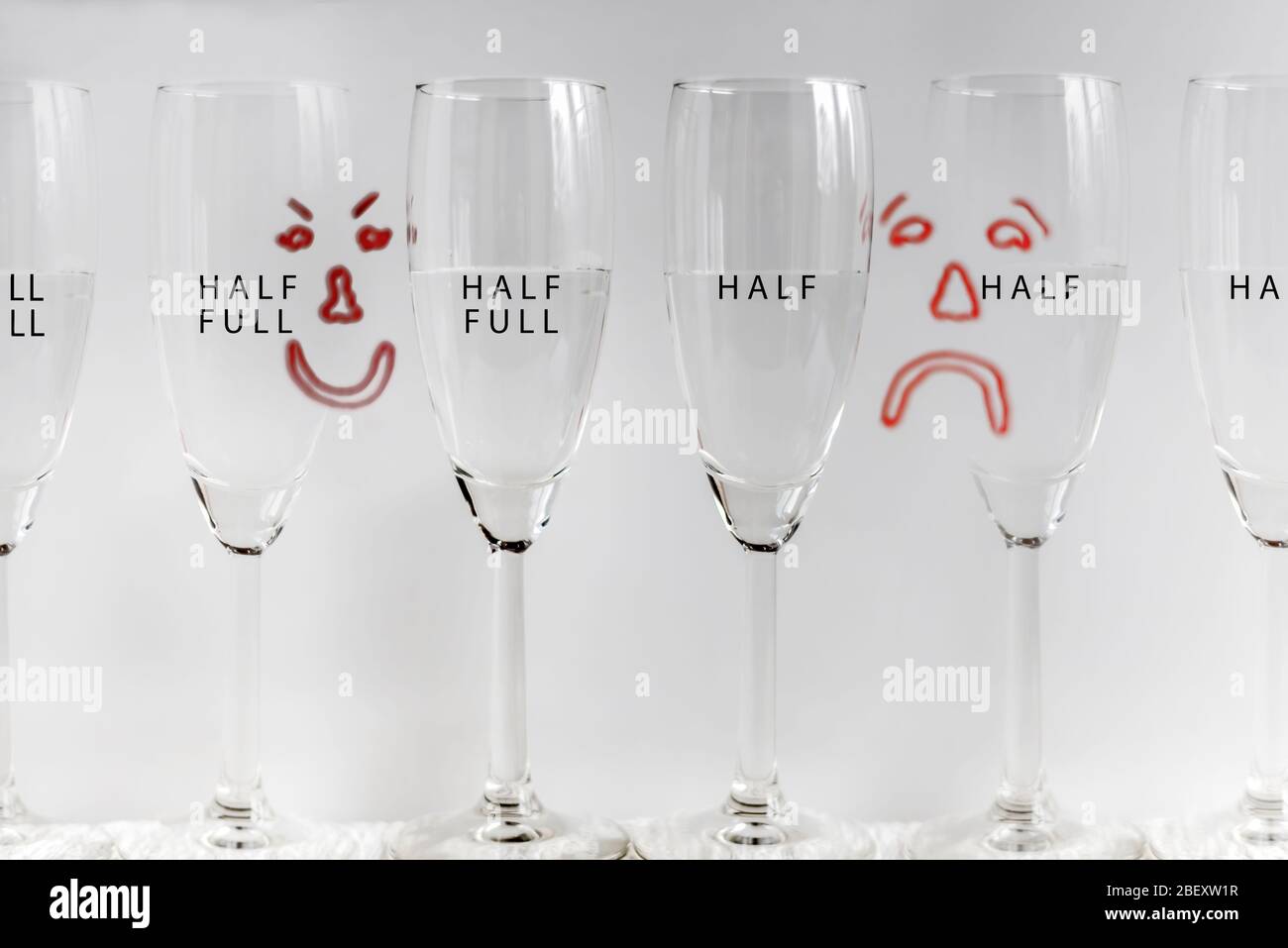 Six wine glasses, half full with drawn sad and happy faces in