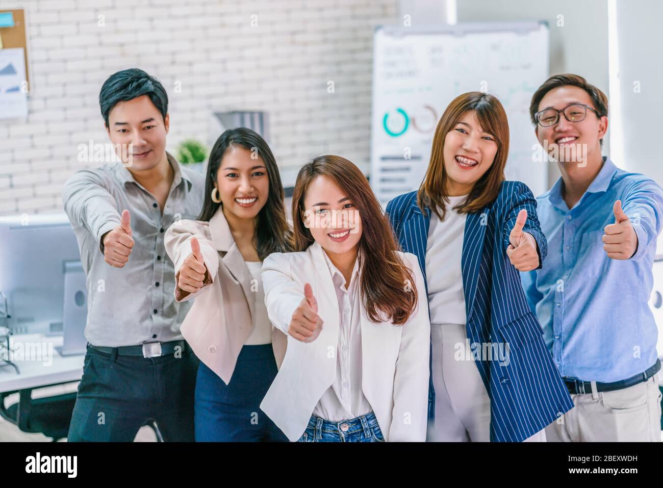 Group of Asian Business people showing thumbs up and looking at camera together at modern workplace, Team work and team building, small business owner Stock Photo