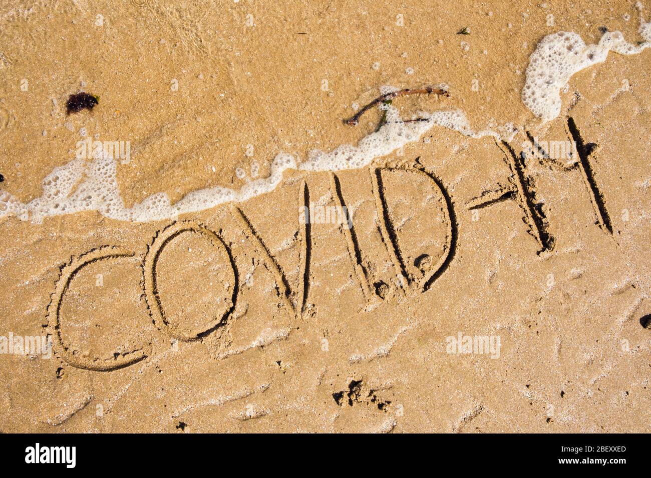 Covid-19 written in sand being washed away by incoming tide.  To illustrate eliminating coronavirus concept. UK, Britain Stock Photo