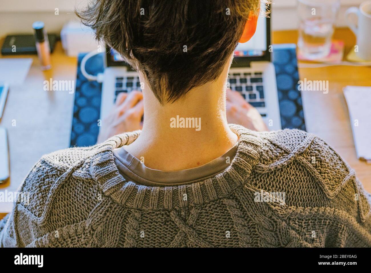 Young caucasian employee woman in sweater sitting and working remote online from home on computer laptop, candid, real photo Stock Photo