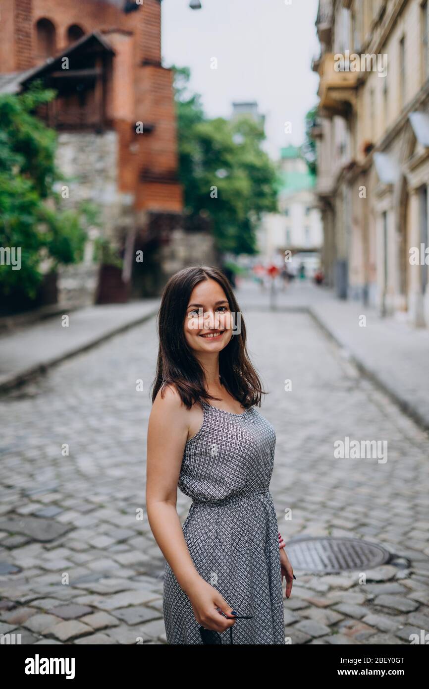 Smiling beautiful girl walking in the city. Brunette girl in summer dress  on city tour. Young woman on a tour views the beautiful streets of the old  c Stock Photo - Alamy