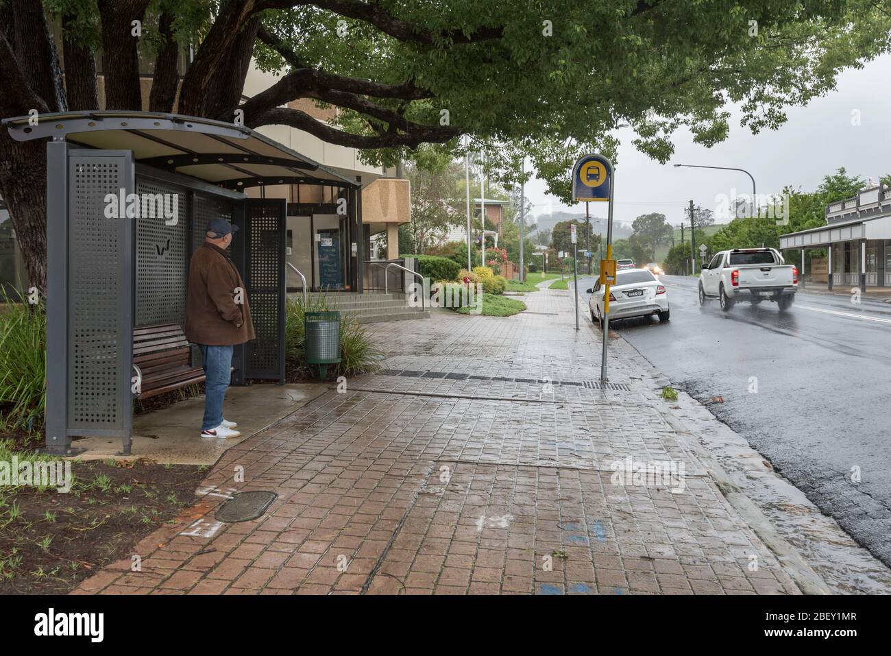 On a rainy day a man stands and waits at a bus stop in the regional town of Picton, New South Wales, Australia Stock Photo