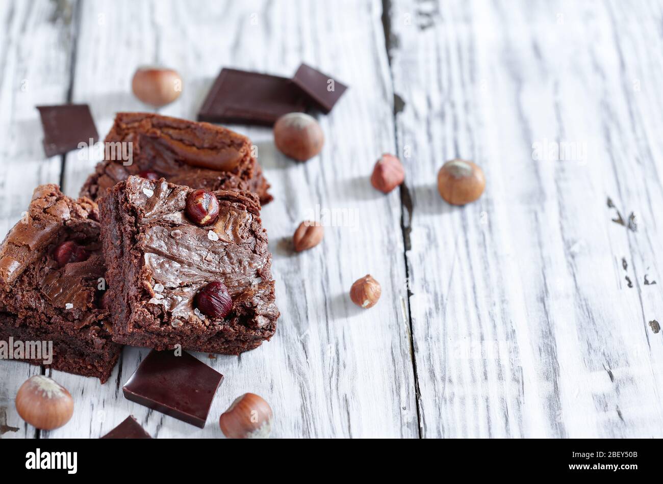 Fresh made homemade brownies made with from chocolate candy and hazelnuts over a a white rustic wooden table. Selective focus with blurred background. Stock Photo