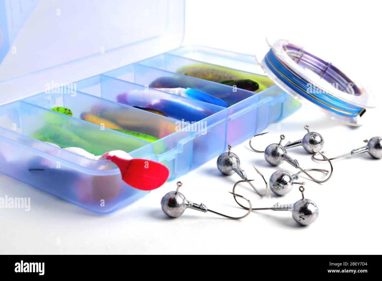 Box for fishing accessories with silicone baits inside, Jig hooks, braided reel on a white background close-up Stock Photo