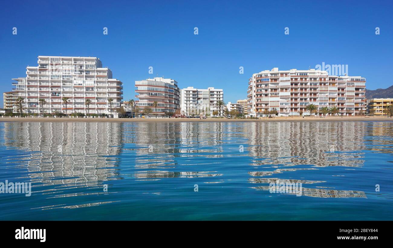 Coastline with apartment buildings along the beach reflected in water surface, Spain, Costa Brava, Mediterranean sea, Roses, Catalonia Stock Photo