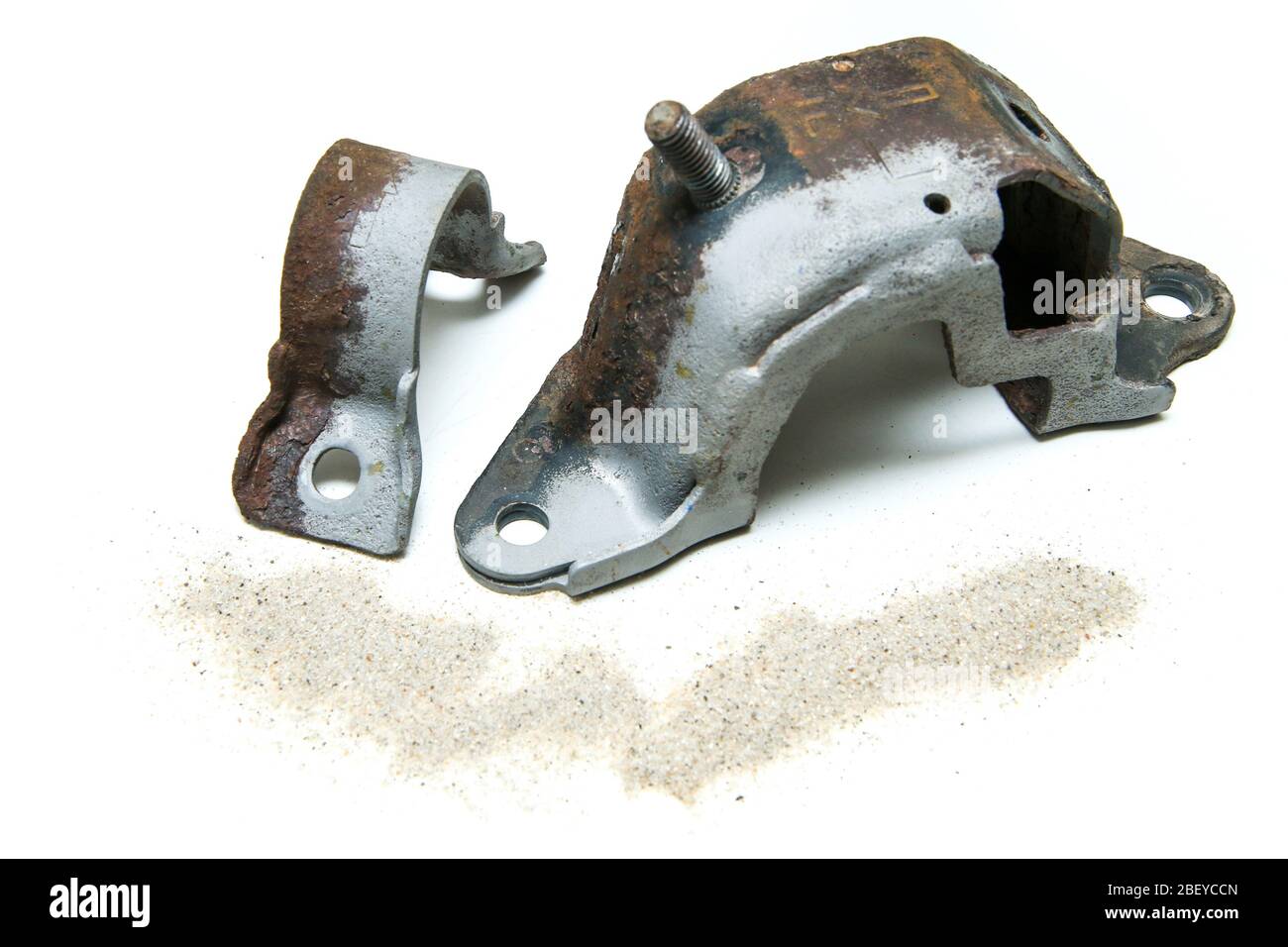 The overgrown rusty cast iron parts partly sand blasted together with sand isolated in a white background. Stock Photo