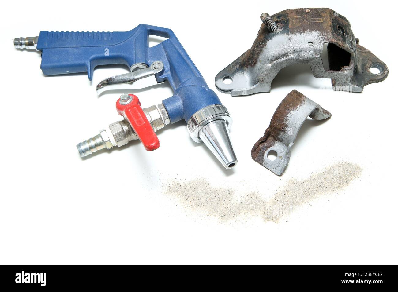 The overgrown rusty cast iron part partly sand blasted together with sand and blasting gun isolated in a white background. Stock Photo