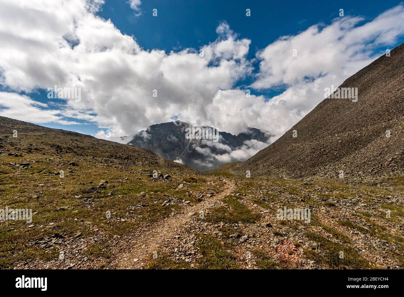 A Rocky Path Between The Mountains Leads To A High Mountain Surrounded By Clouds Lots Of Stones On The Ground Blue Sky And Low Clouds Horizontal Stock Photo Alamy