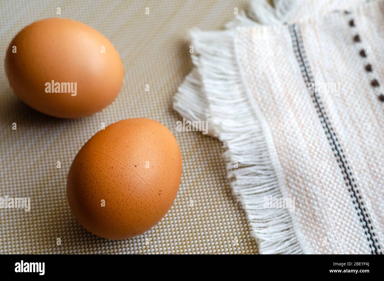 Two brown chicken eggs and a kitchen towel. Closeup of uncooked farm eggs on beige. A folded towel and a pair of eggs. Top view at an angle. Selective Stock Photo