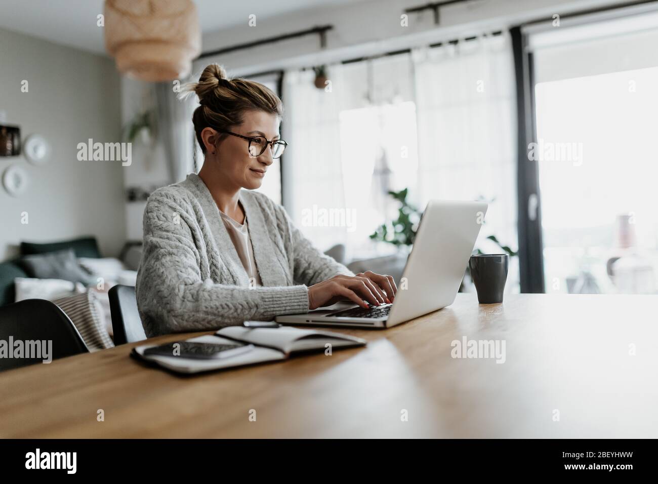 Businesswoman working on laptop computer sitting at home and managing her business via home office during Coronavirus or Covid-19 quarantine Stock Photo