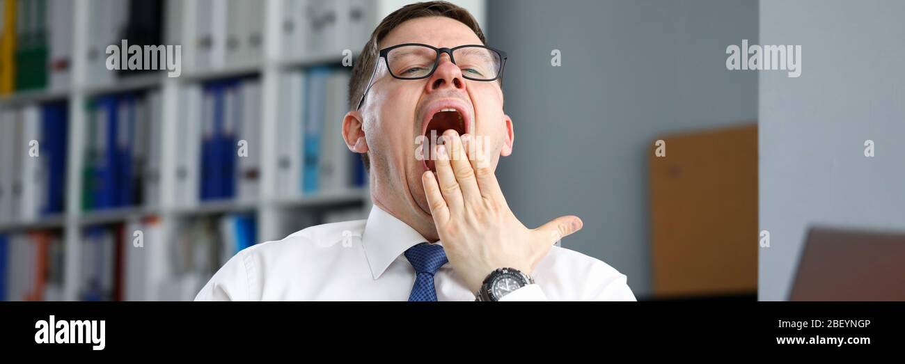 Tired businessman office sits at table and yawns Stock Photo