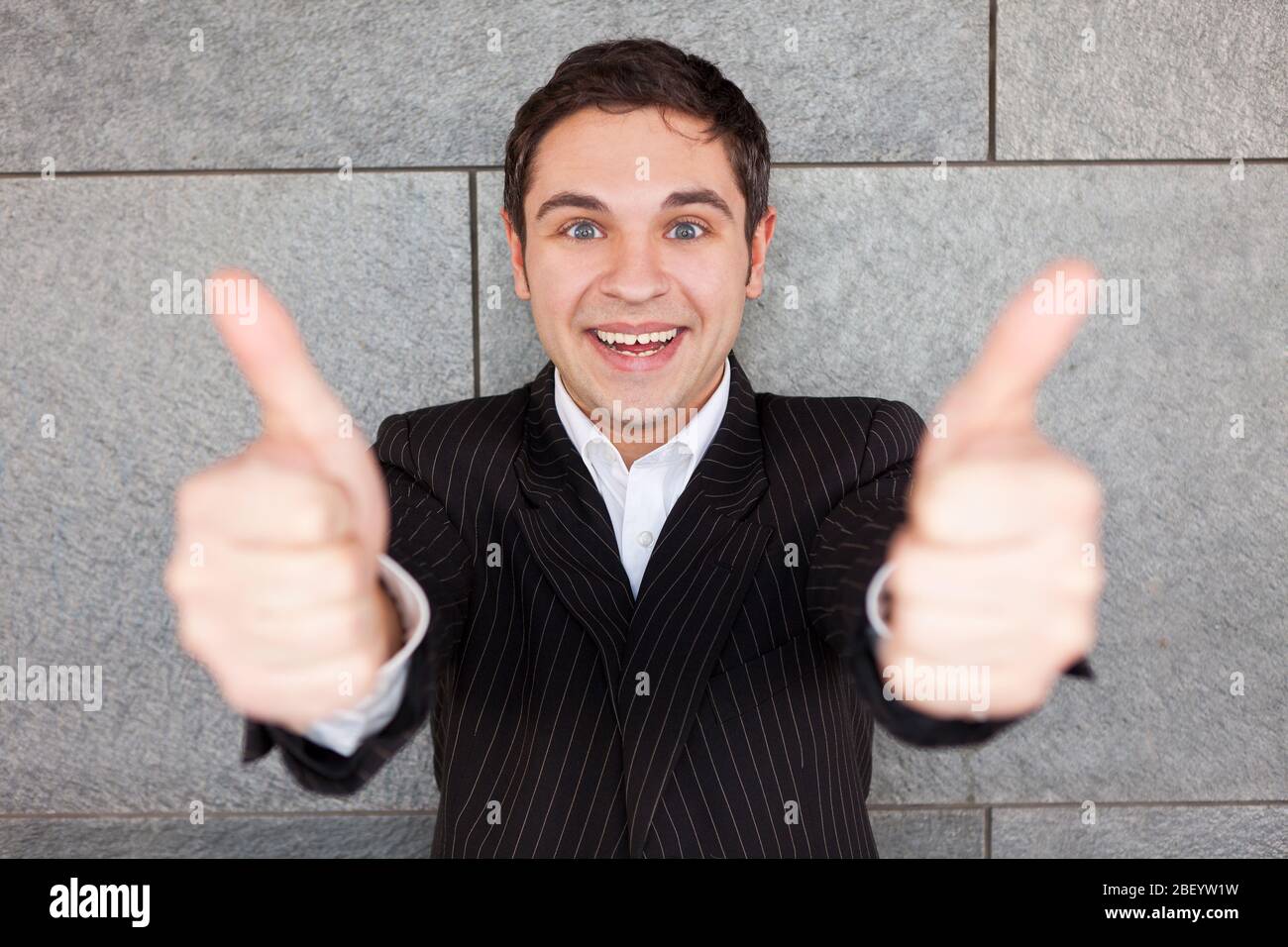 Laughing manager leaning against wall holds both thumbs up Stock Photo