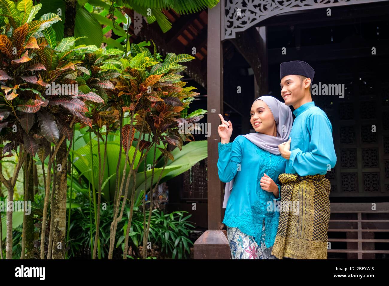 A portrait of young couple of malay muslim in traditional costume during Aidilfitri celebration by traditional wooden house. Raya and Muslim fashion a Stock Photo