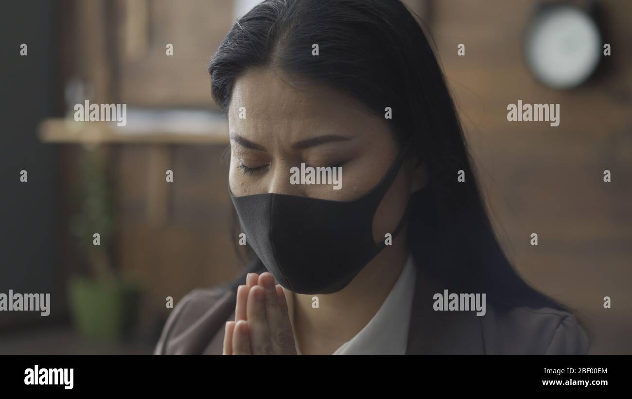 Asian Woman In Mask Praying In Isolation During Epidemic Stock Photo