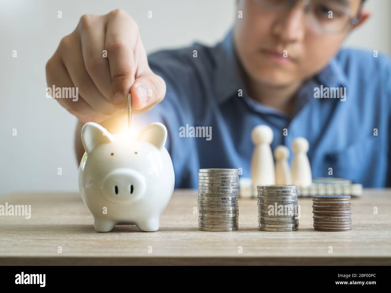 Money savings concepts  piggy bank and stack coins with blur Men are coining in piggy bank for saving money for families with family wooden dolls Stock Photo