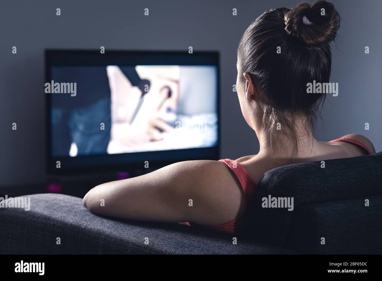 Young woman watching horror movie on online stream service. Girl streaming scary film or series at night. Fear and terror during thriller on tv. Stock Photo
