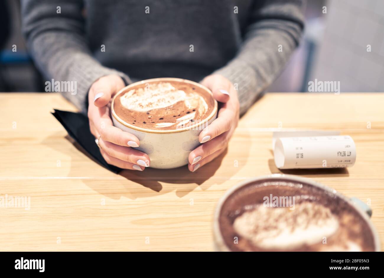 Coffee cup between hands in cafe in winter. Cappuccino, macchiato, latte or hot chocolate cocoa. Two persons having a warm meeting or date. Stock Photo