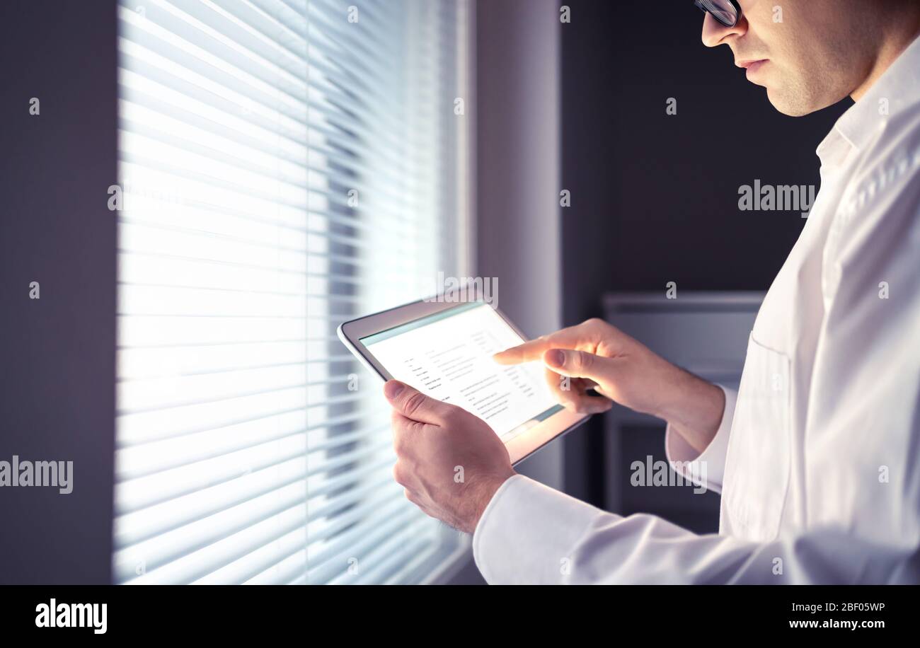 Doctor or business man using tablet. Electronic medical record or email messages on screen. Serious thoughtful person with stress working late. Stock Photo