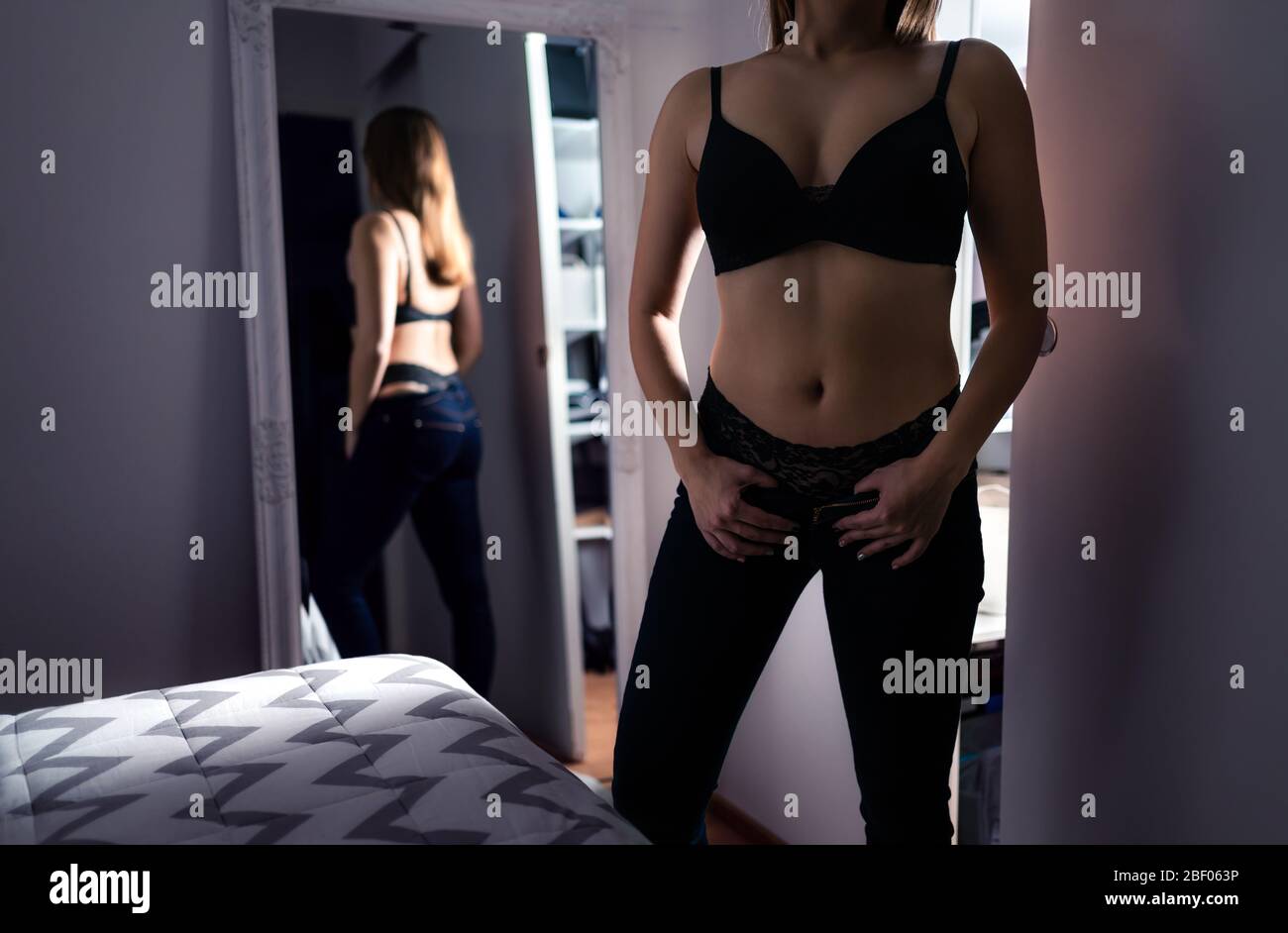 Seductive woman in underwear. Sexy fashion model in black bra and lingerie. Erotic girl in home bedroom at night in dark. Elegant lifestyle. Stock Photo