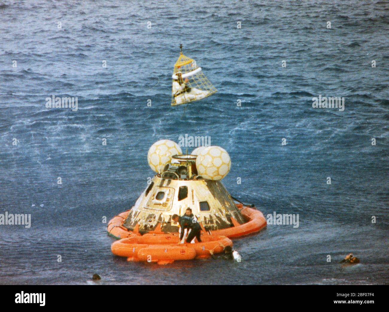 Astronaut John L. Swigert Jr., command module pilot, is lifted aboard a helicopter in a Billy Pugh helicopter rescue net while astronaut James A. Lovell Jr., commander, awaits his turn. The crew was taken to the U.S.S. Iwo Jima, prime recovery ship, several minutes after the Apollo 13 spacecraft splashed down at 12:01:44 pm CST on April 17, 1970. Stock Photo