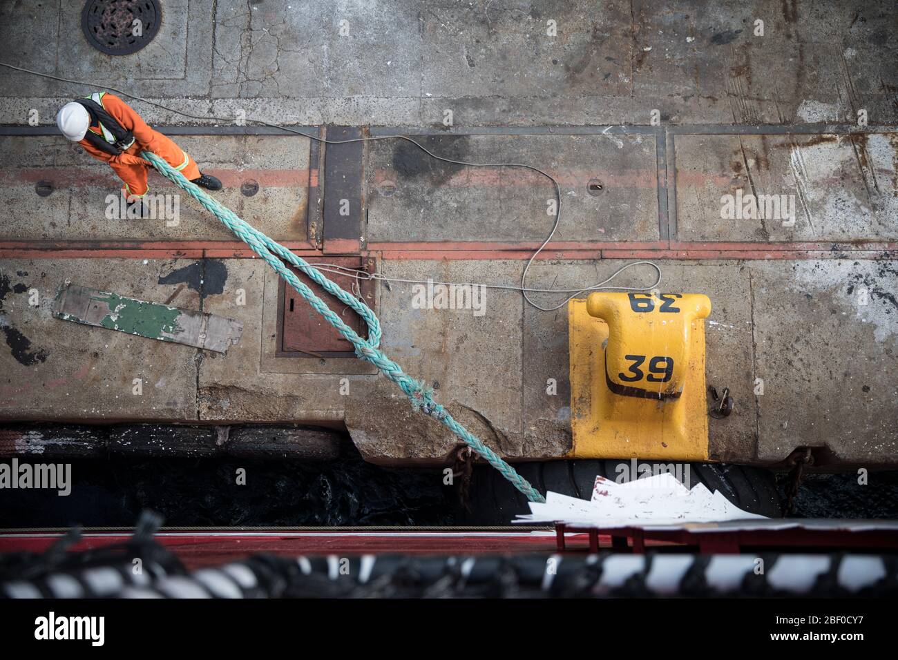 A dock worker unties a ship from a cleat in the port of Cape Town, Western Cape, South Africa, a busy trade route, as it readies to set sail. Stock Photo