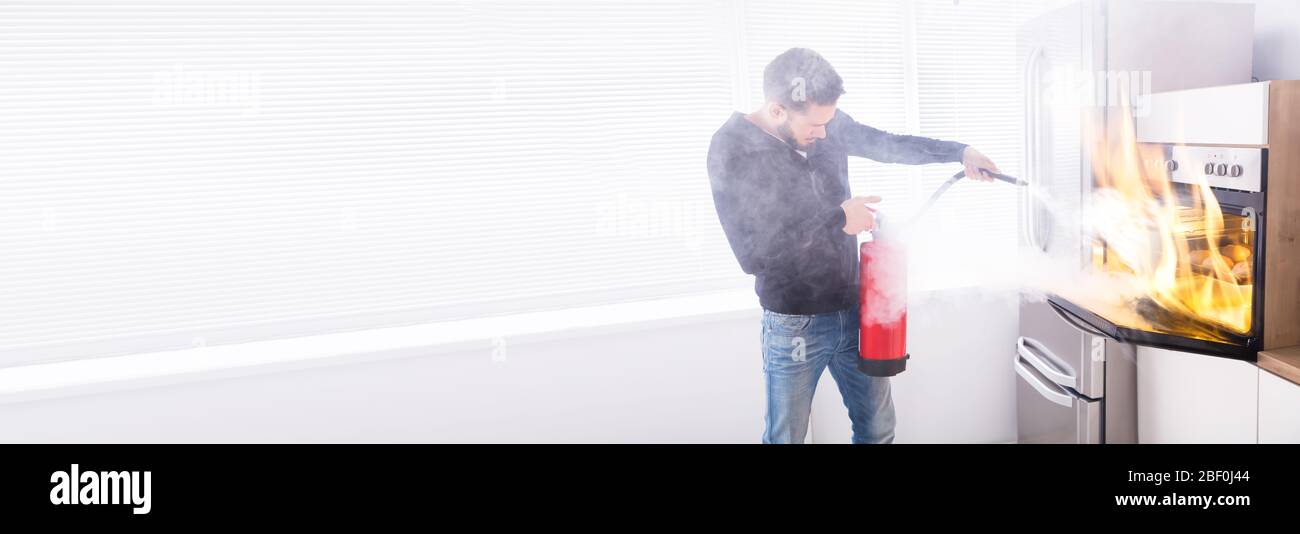 Man Using Fire Extinguisher On Oven In Kitchen Stock Photo Alamy