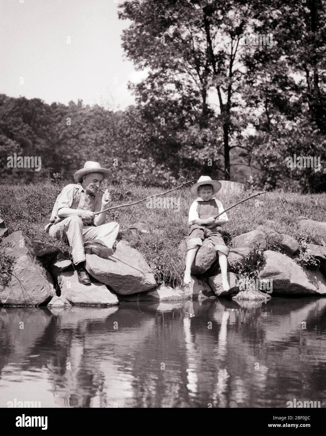 1930s BOY FISHING IN POND WITH HIS GRANDFATHER USING FISHING RODS MAKE FROM TWIGS - a4789 HAR001 HARS FRIENDSHIP HALF-LENGTH PERSONS MALES SENIOR MAN SENIOR ADULT B&W HAPPINESS OLDSTERS OLDSTER HIS PIPES TOBACCO RECREATION BAD HABIT SMOKER USING ELDERS NICOTINE CONNECTION GRANDFATHERS STRAW HAT ADDICTIVE GRANDSON TWIGS ANGLING COOPERATION CORNCOB GROWTH JUVENILES RELAXATION RODS TOGETHERNESS BLACK AND WHITE CAUCASIAN ETHNICITY GRANDPA HAR001 OLD FASHIONED Stock Photo