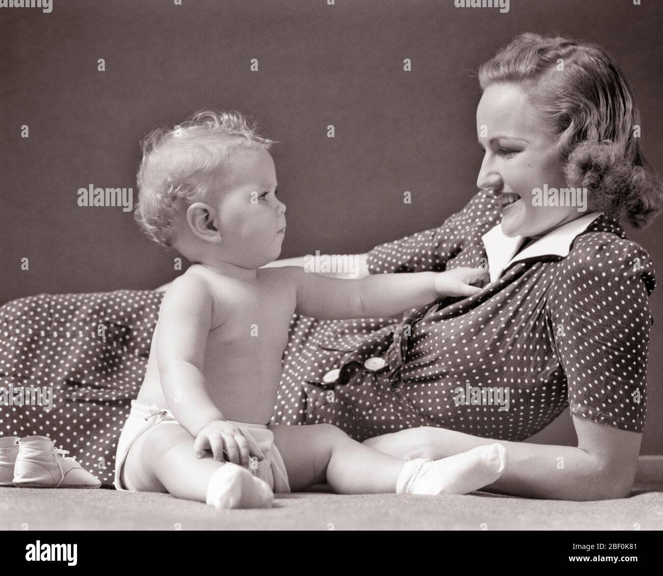 1930s 1940s BLONDE BABY GIRL IN CLOTH DIAPER SITTING UP REACHING OUT TO TOUCH SMILING RECLINING MOTHER WEARING POLKA DOT DRESS - b1631 HAR001 HARS INFANT TOUCH STRONG PLEASED FAMILIES JOY LIFESTYLE SATISFACTION FEMALES STUDIO SHOT HEALTHINESS HOME LIFE COPY SPACE FRIENDSHIP HALF-LENGTH LADIES DAUGHTERS PERSONS CARING B&W DOT HAPPINESS CHEERFUL DISCOVERY POLKA POLKA DOTS PRIDE UP REACH SMILES CONNECTION POLKA DOT JOYFUL STYLISH PERSONAL ATTACHMENT AFFECTION EMOTION GROWTH JUVENILES MOMS TOGETHERNESS YOUNG ADULT WOMAN BABY GIRL BLACK AND WHITE CAUCASIAN ETHNICITY HAR001 OLD FASHIONED Stock Photo