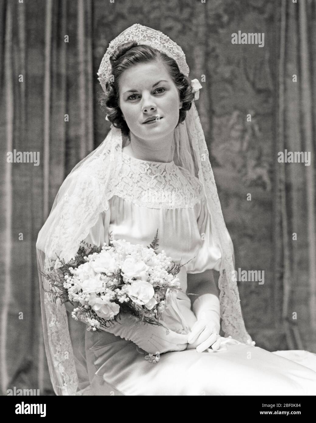 1930s PORTRAIT OF SEATED BRIDE WEARING GOWN VEIL HOLDING BOUQUET LOOKING AT CAMERA - b14929 HAR001 HARS COPY SPACE FRIENDSHIP HALF-LENGTH LADIES MARRIAGE PERSONS INSPIRATION SATIN VEIL CEREMONY B&W BRIDAL EYE CONTACT BRUNETTE HAPPINESS BRIDES CUSTOM EXCITEMENT TRADITION NUPTIAL NUPTIALS OCCASION MARRYING PRIDE WHITE  CONCEPTUAL HEADPIECE LILY OF THE VALLEY RITE OF PASSAGE STYLISH WED MARRY MATRIMONY YOUNG ADULT WOMAN BLACK AND WHITE CAUCASIAN ETHNICITY HAR001 OLD FASHIONED Stock Photo