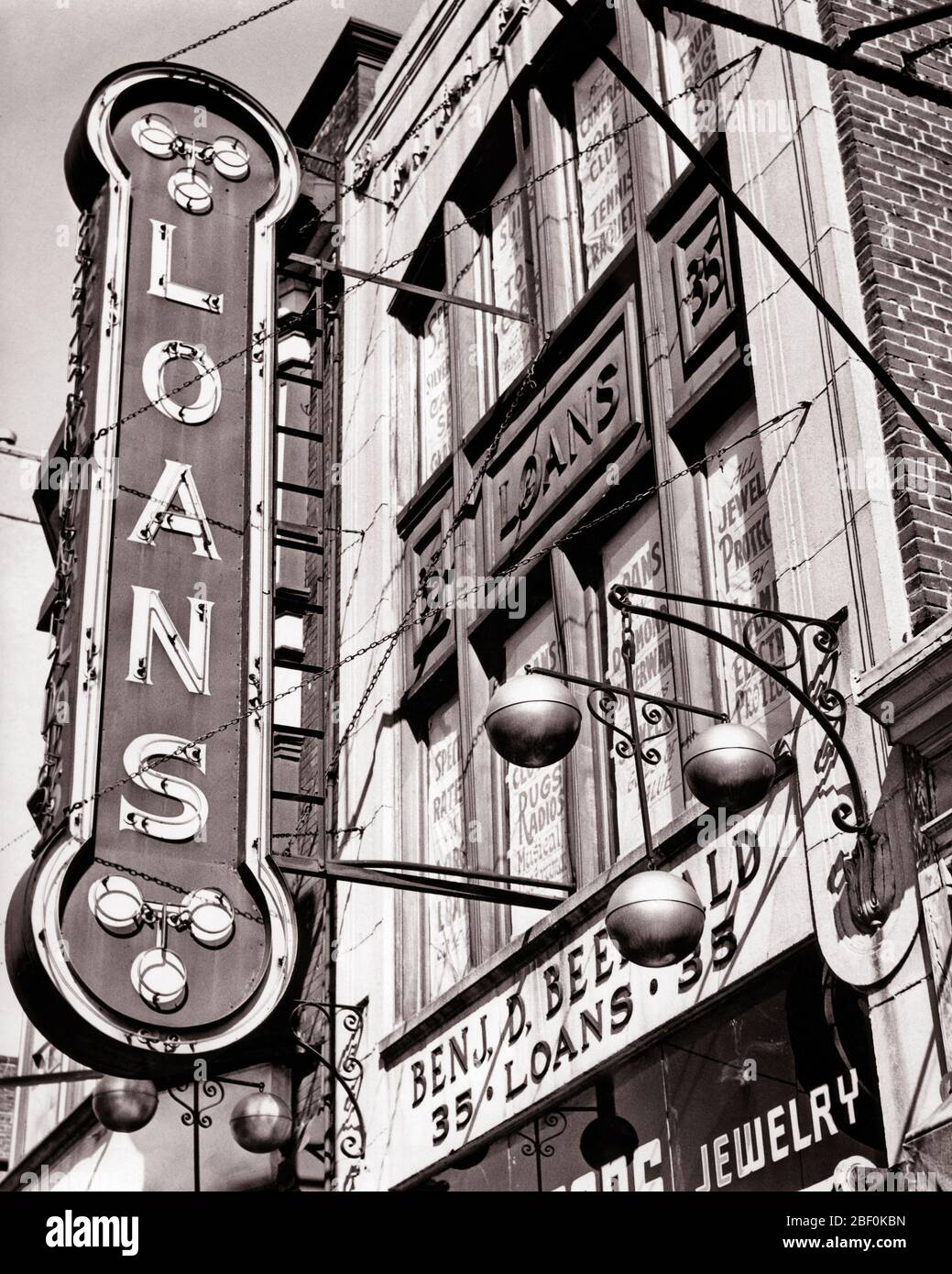 1940s PAWNBROKERS SHOP WITH NEON SIGN  FOR LOANS AND SYMBOL OF THREE GOLD SPHERES SUSPENDED FROM A BAR - b1855 HAR001 HARS AND EXTERIOR LOW ANGLE OCCUPATIONS REAL ESTATE CONCEPT CONCEPTUAL STRUCTURES STOREFRONT EDIFICE PAWNBROKERS SYMBOLIC CONCEPTS BLACK AND WHITE HAR001 LOANS OLD FASHIONED PAWN REPRESENTATION SUSPENDED Stock Photo
