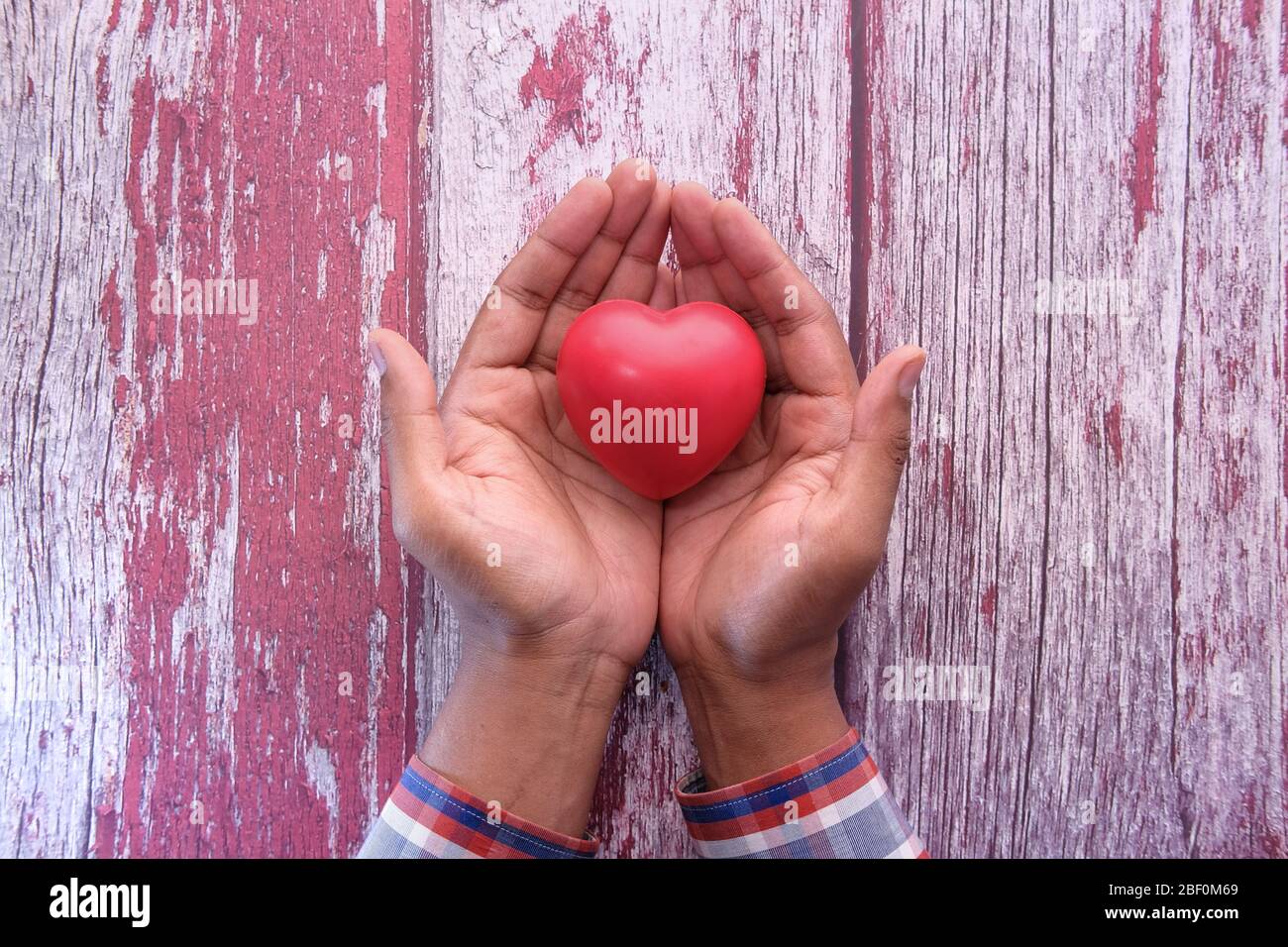 man holding red heart in hands on wooden table . Stock Photo