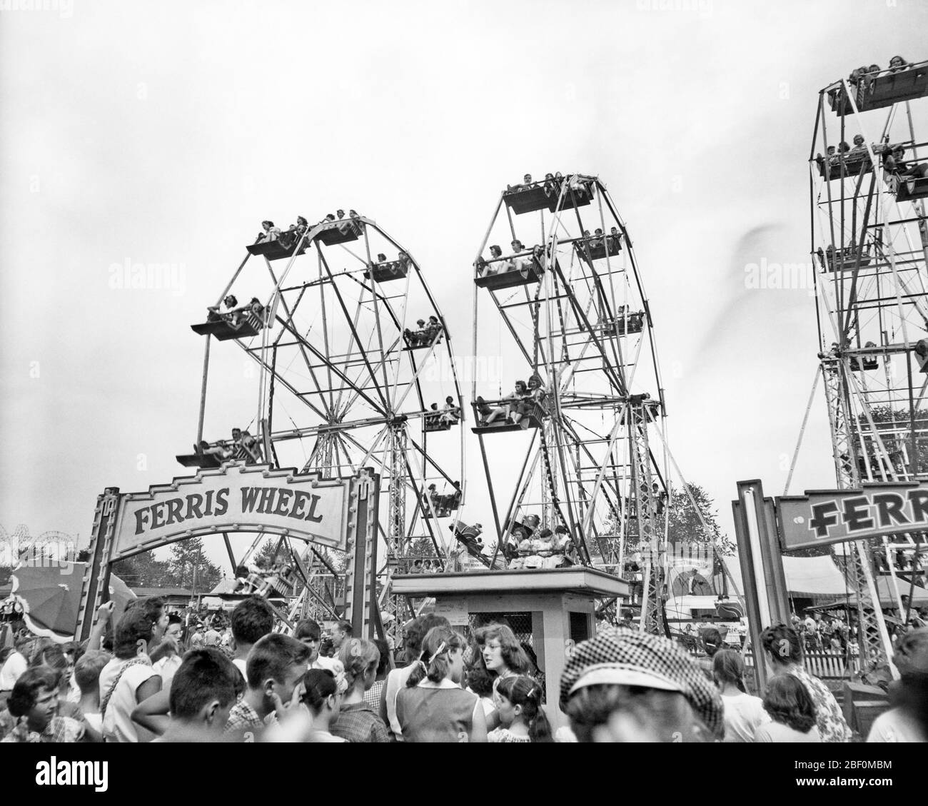 1960s TEENS LINED UP AT TICKET BOTH TO RIDE ON ONE OF THREE FERRIS WHEELS AT COUNTY FAIR - f11220 HAR001 HARS THEME PARK Stock Photo