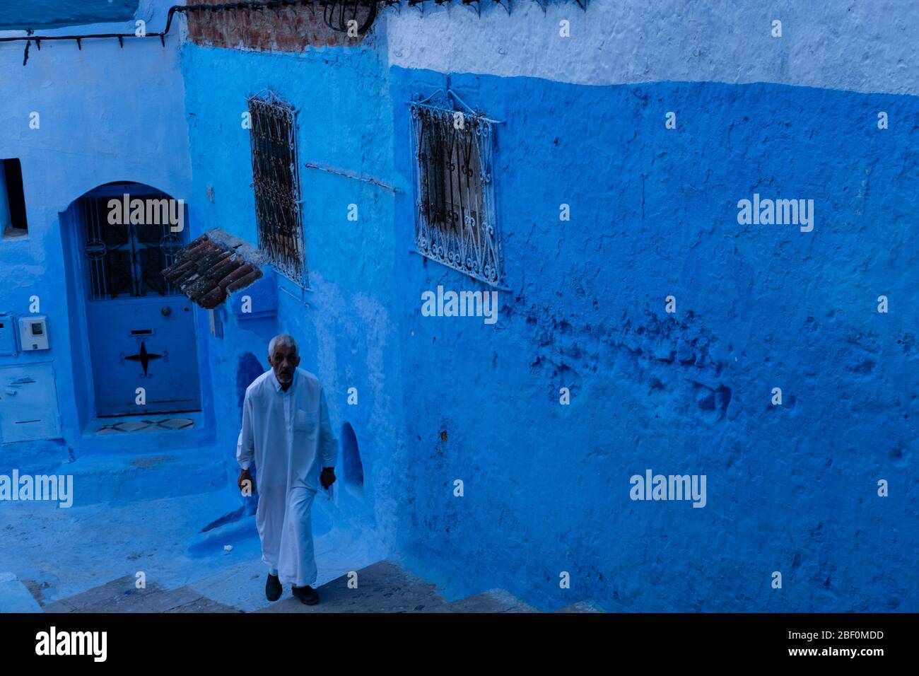 Chefchaouen, northern Morocco, June 10, 2016. An old man, in traditional Moroccan dress, on a staircase in one of the streets of the blue city. Stock Photo