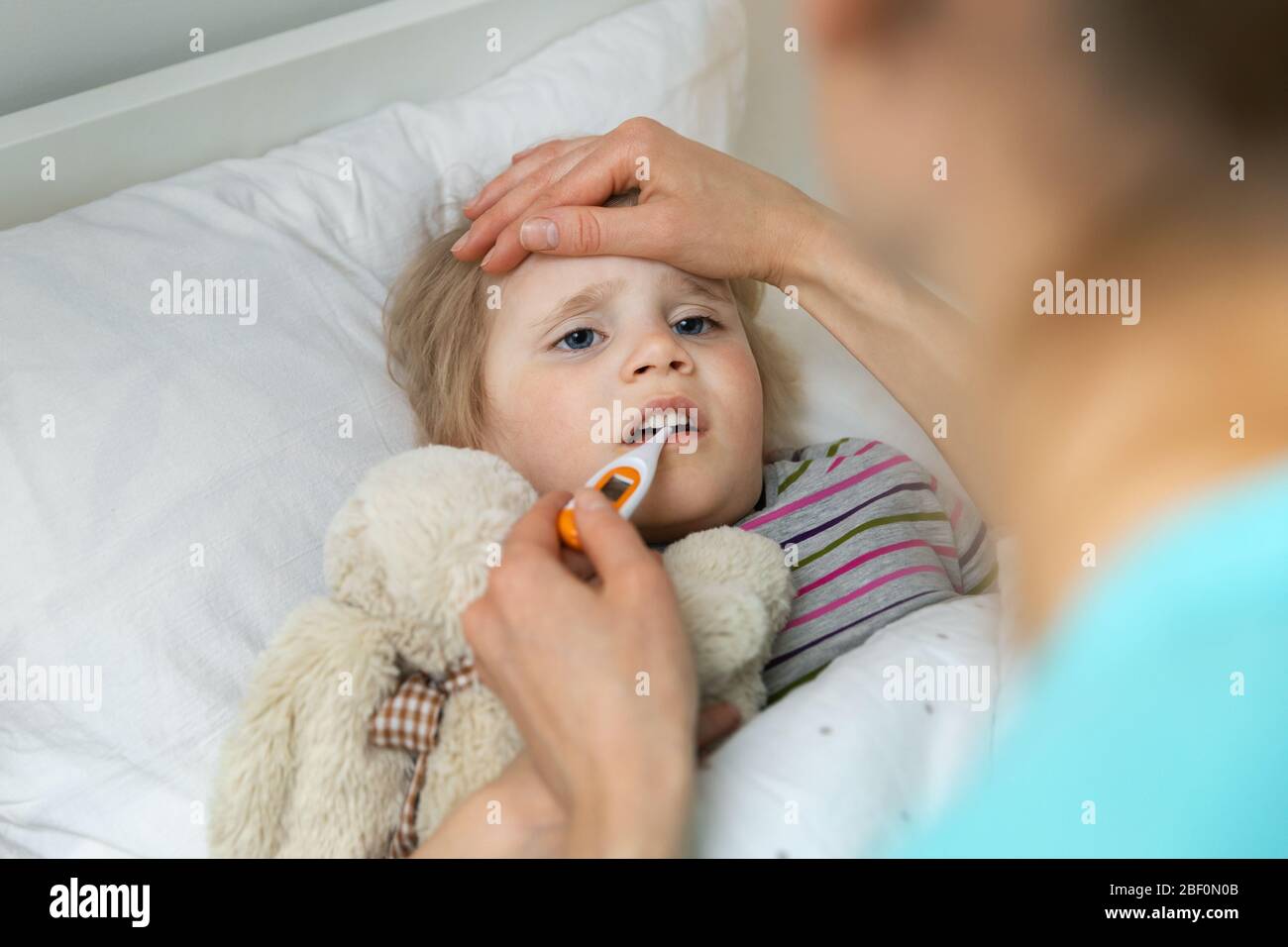 mother comforting her sick child and measuring temperature in bed at home Stock Photo