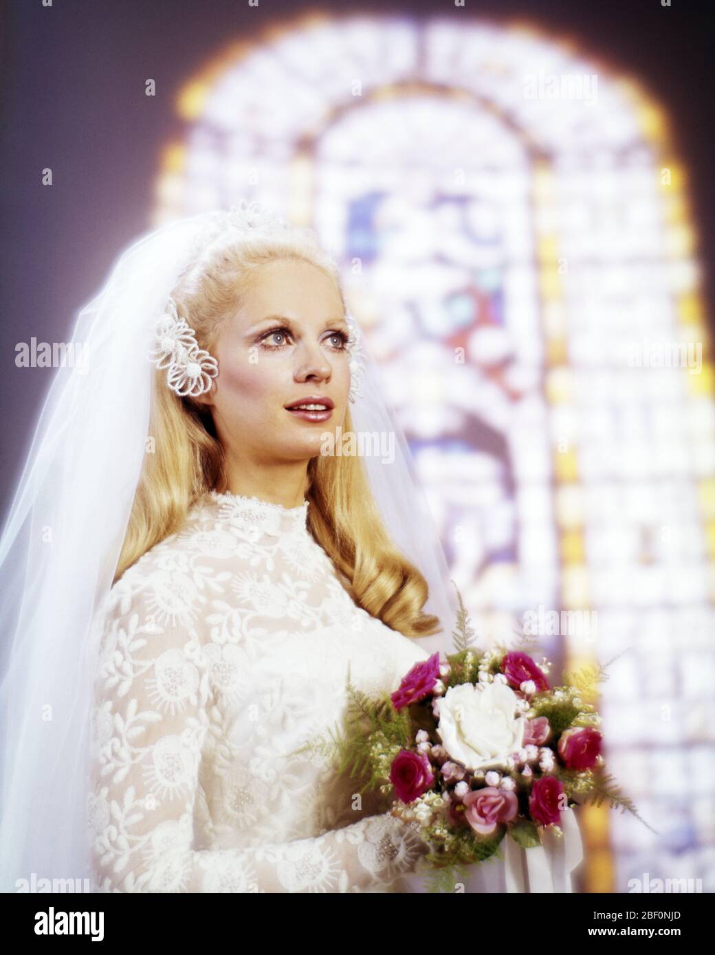 1960s BLONDE WOMAN BRIDE WEARING LACE BRIDAL GOWN NET VEIL HOLDING RED AND WHITE BOUQUET  IN FRONT OF STAINED GLASS WINDOW - kb9221 PHT001 HARS MARRIED STUDIO SHOT EVENT COPY SPACE FULL-LENGTH LADIES MARRIAGE PERSONS VEIL CONFIDENCE CEREMONY BRIDAL DREAMS BRIDES RELIGIOUS CUSTOM AND TRADITION NUPTIAL NUPTIALS OCCASION MARRYING PRIDE HEADPIECE RITE OF PASSAGE STYLISH WED FAITHFUL FAITH LOOKING UP MARRY MATRIMONY YOUNG ADULT WOMAN BELIEF CAUCASIAN ETHNICITY OLD FASHIONED Stock Photo