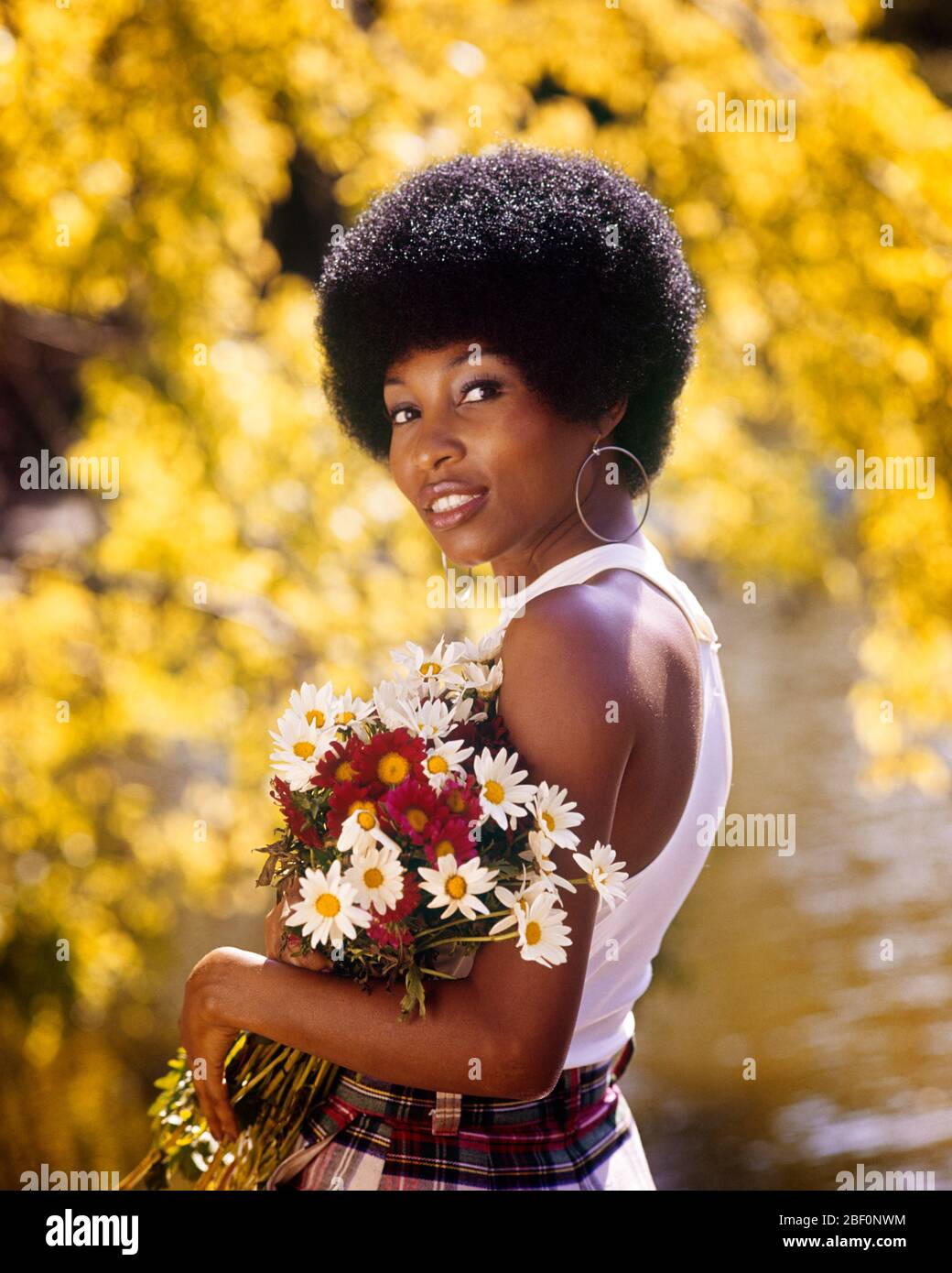 1970s SMILING AFRICAN AMERICAN WOMAN WEARING HOOP EARRINGS WHITE TANK TOP HOLDING A BOUQUET SPRING FLOWERS LOOKING AT CAMERA - kg6614 PHT001 HARS ETHNIC BLACK LOOKING BACK PRIDE SMILES STYLISH TANK TOP HOOP EARRINGS PEOPLE ADULTS UNIVERSITY COED YOUNG ADULT WOMAN AFRO HAIR STYLE OLD FASHIONED AFRICAN AMERICANS Stock Photo